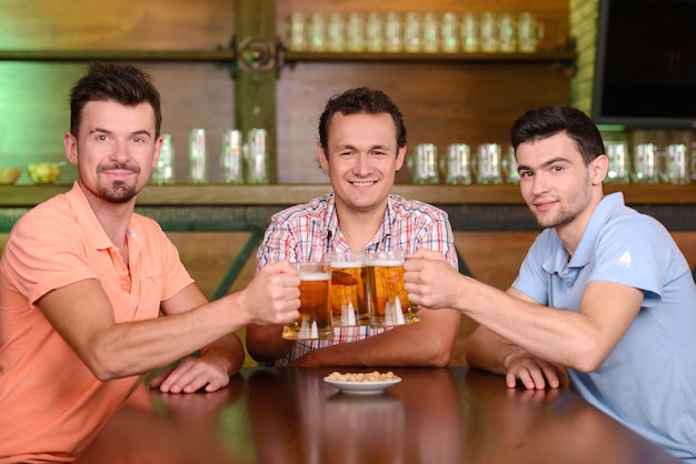 Drei glückliche Freunde, die Bier an der Kneipe trinken.