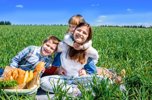 Drei glückliche Kinder sitzen auf Picknick auf dem Feld. blauer Himmel, grünes Gras. Brot, Kuchen und Obst in einem Korb.