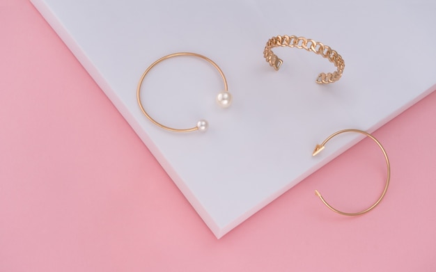 Drei goldene Armbänder auf rosa und weißem Papierhintergrund mit Kopienraum