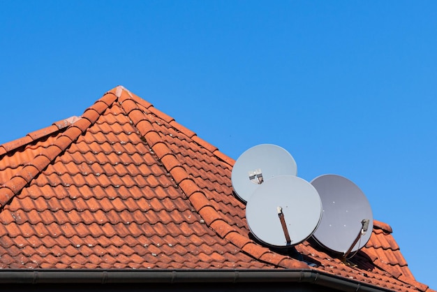 Drei graue Satellitenschüsseln auf dem Dach eines mit Ziegeln gedeckten Hauses