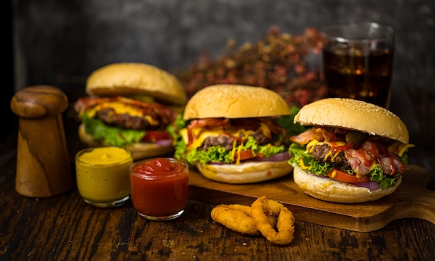 Drei Hamburger mit Rindfleischburger, gebratenen Zwiebeln, Spinat, Ketchup, Pfeffer und Käse serviert auf einem Holzbrettboden mit Softdrink.