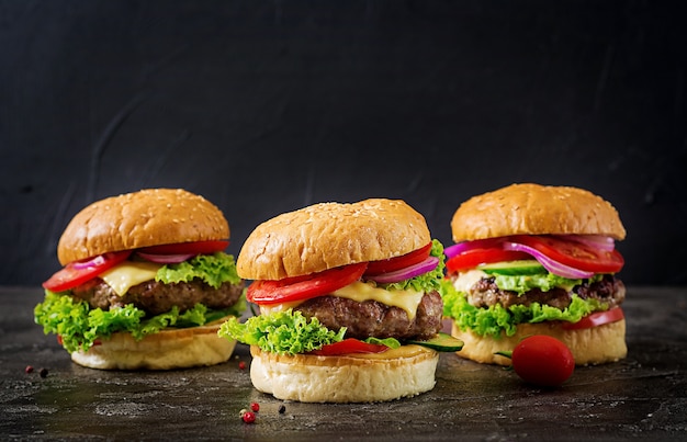 Drei Hamburger mit Rindfleischfleischburger und Frischgemüse auf dunklem Hintergrund.