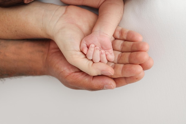 Drei Handflächen einer glücklichen Familie. Kleine neugeborene Hand mit winzigen Fingern. Die Handfläche von Eltern, Vater und Mutter hält den Griff eines Neugeborenen. Studio-Makroaufnahme auf weißem Hintergrund