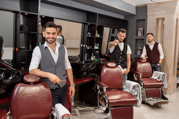 Drei hübsche Friseure, die im Friseursalon nahe Friseurstühlen aufwerfen.