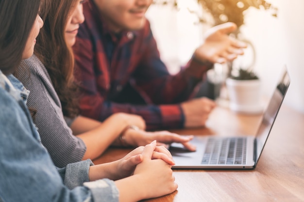 Drei junge Asiaten, die während eines Meetings denselben Laptop verwenden und betrachten