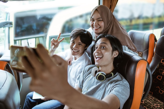 Drei junge Asiaten lächeln und posieren vor ihrer Handykamera, während sie gemeinsam im Bus ein Selfie machen