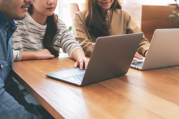 Drei junge asiatische Leute, die zusammen Laptop-Computer auf Holztisch benutzen und betrachten