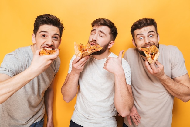 Drei junge entzückte Männer, die Pizza essen