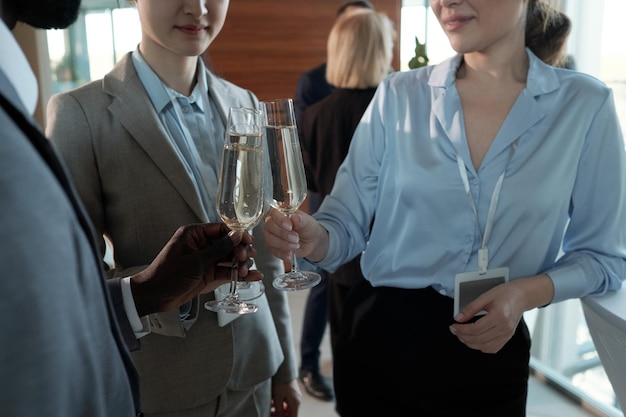 Drei junge, erfolgreiche Maklerinnen in Abendgarderobe, die mit Champagner klirren