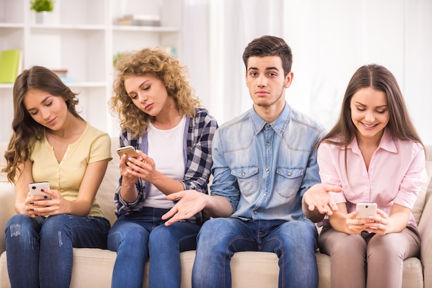 Drei junge Frauen, die am Sofa sitzen und ihre Telefone verwenden.