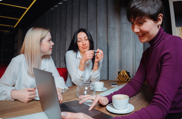 Drei junge Geschäftsfrauen, die mit Laptop am Tisch sitzen und an einem Projekt im Café arbeiten. Teamwork, Geschäftstreffen. Freiberufler arbeiten.