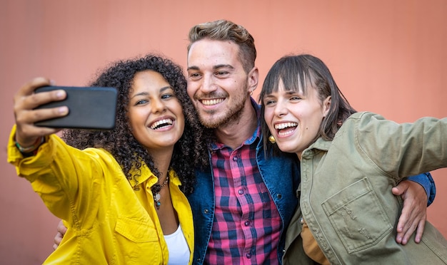 Drei junge glückliche Freunde, die Selfie mit einem Smartphone im Freien in der Stadt machen, z