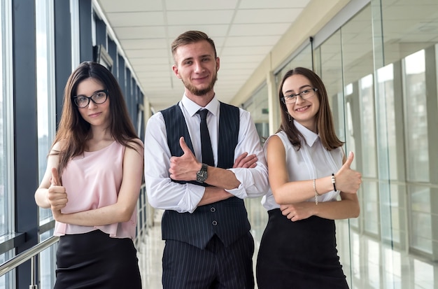 Drei junge glückliche Geschäftspartner, die Vertrag oder Bericht besprechen, während sie im Büroflur stehen.