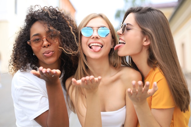 Drei junge lächelnde Hippie-Frauen in Sommerkleidung, die auf der Straße aufwirft. Weiblich, das positive Gesichtsgefühle zeigt.