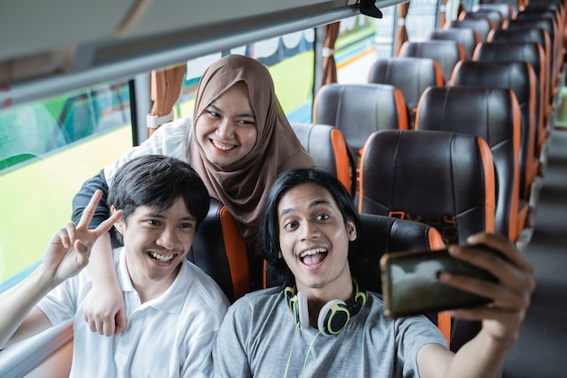 Drei junge Leute lächeln und posieren vor ihrer Handykamera, während sie gemeinsam ein Selfie im Bus machen