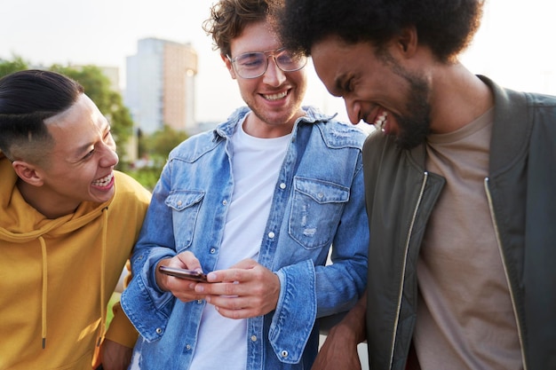 Drei junge Männer lachen über etwas, das ein Mobiltelefon in der Hand hält