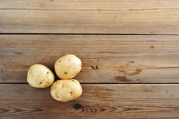 Drei junge rohe weiße Kartoffeln auf rustikalem hölzernem Hintergrund