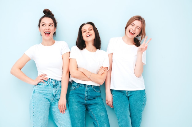 Drei junge schöne lächelnde Hipster-Frau in trendigen weißen T-Shirts und Jeans im gleichen Sommer