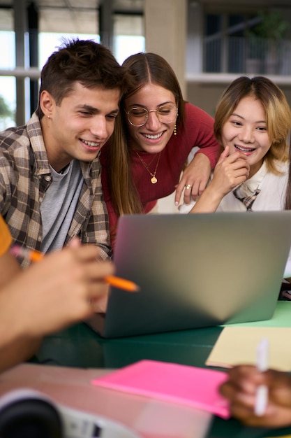 Drei junge Universitätsstudenten versammelten sich zusammen mit einem Laptop in der Studienhalle des Campus.