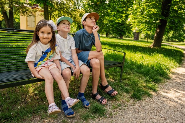 Drei Kinder, die in der Bank am Park sitzen Zwei Brüder und Schwester