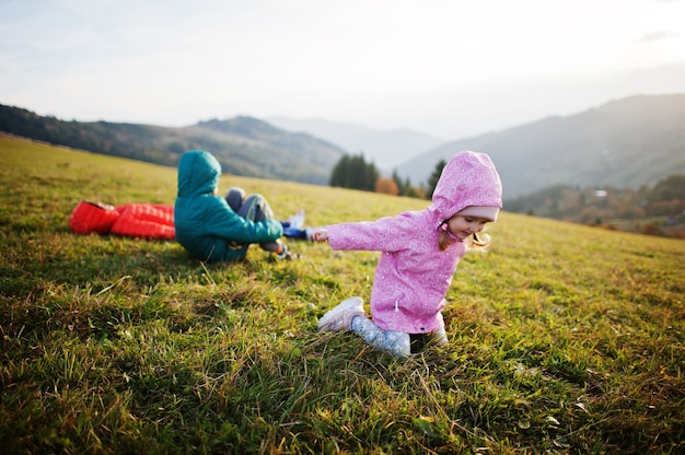 Drei Kinder liegen im Gras mit einer wunderschönen Bergkette am Horizont.