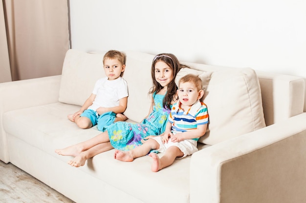 Drei Kinder sitzen auf einem hellen Sofa. Schwester und ihre beiden jüngeren Brüder im Wohnzimmer.