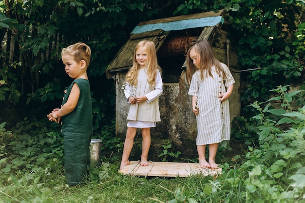 Drei Kinder spielen in der Nähe des Brunnens auf einem Hintergrund aus Gras und Bäumen