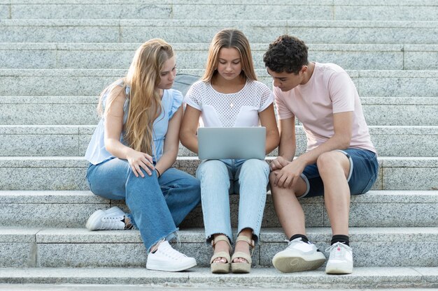 Drei Klassenkameraden sitzen auf Treppen und arbeiten gemeinsam an einem Laptop Teamwork im Jugendkonzept