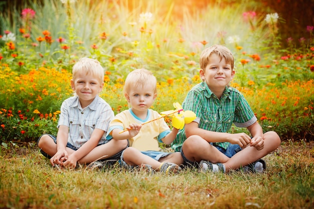 Drei kleine Brüder, die auf Gras am sonnigen Sommertag sitzen.