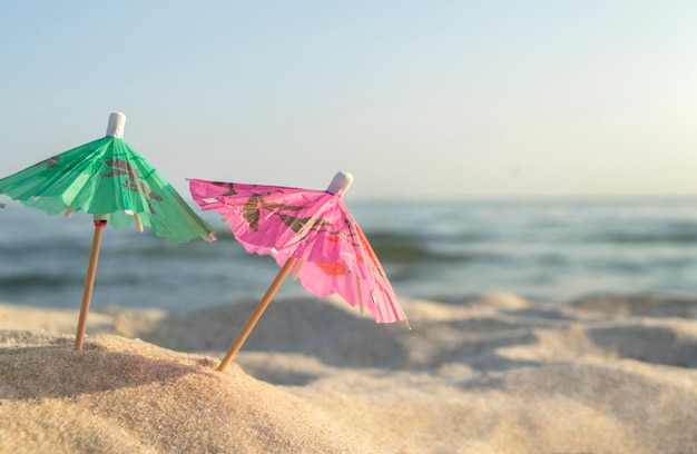 Drei kleine Cocktailschirme aus Papier stehen im Sand am Sandstrand in der Nähe