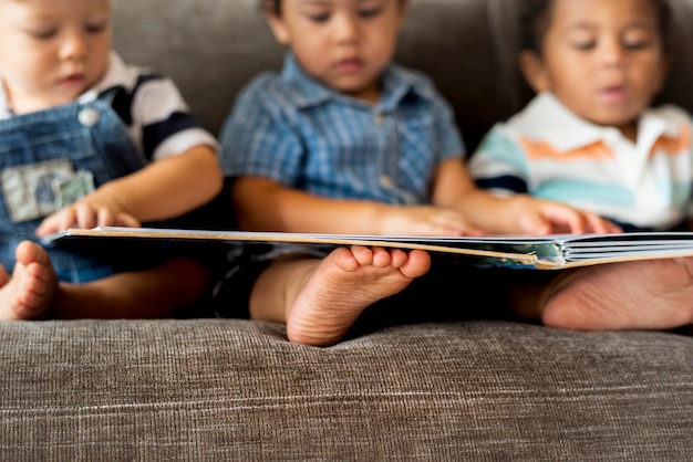 Drei kleine Jungen, die ein Buch auf einem Sofa lesen