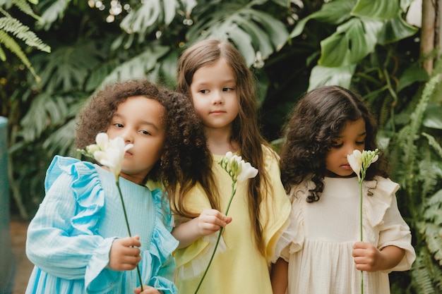 Drei kleine Mädchen im Garten mit Blumen in ihren Händen Kinder verschiedener Nationalitäten