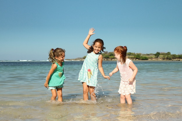 Drei kleine Mädchen spielen am Strand unter dem blauen Himmel des Sommers