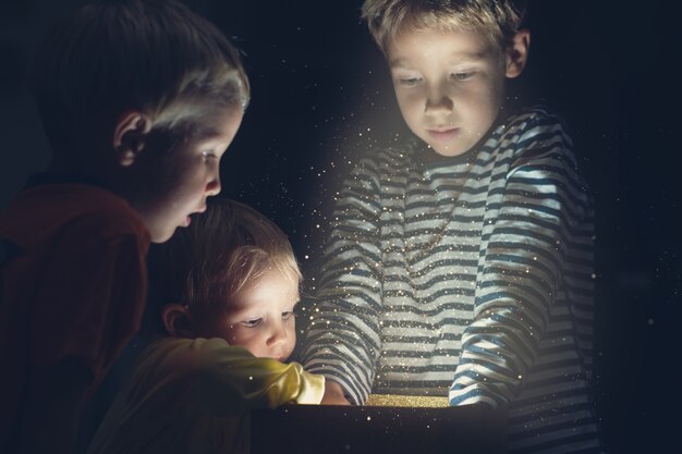 Drei Kleinkindkinder greifen in eine goldene Geschenkbox mit funkelndem Licht und Glitzern.