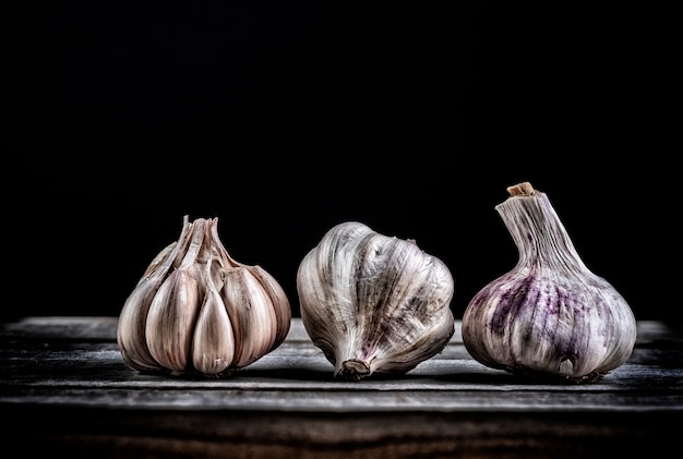 Drei knoblauch in verschiedenen positionen auf holzbrett auf schwarzem hintergrund