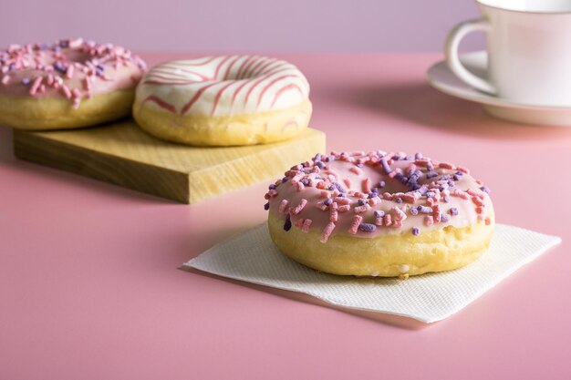 Drei köstliche frisch geglasierte Donuts und eine Porzellanbecher für Kaffee oder Tee auf rosa Hintergrund