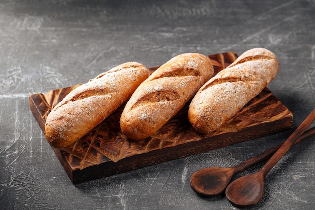 Drei Laibe frisch gebackenes Baguette auf dem hölzernen Schneidebrett auf grauem Hintergrund