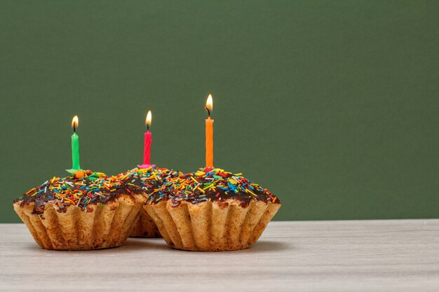 Drei leckere Geburtstagskuchen mit Schokoladenglasur und Karamell, dekoriert mit brennenden festlichen Kerzen auf grünem Hintergrund mit Kopierraum. Alles Gute zum Geburtstag minimales Konzept.