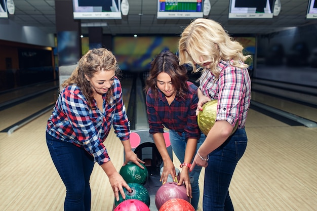 Foto drei lustige attraktive freundinnen nehmen bowlingkugeln