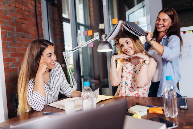 Drei lustige junge studenten, die spaß haben, während sie am schreibtisch sitzen und sich auf die prüfung im arbeitszimmer vorbereiten