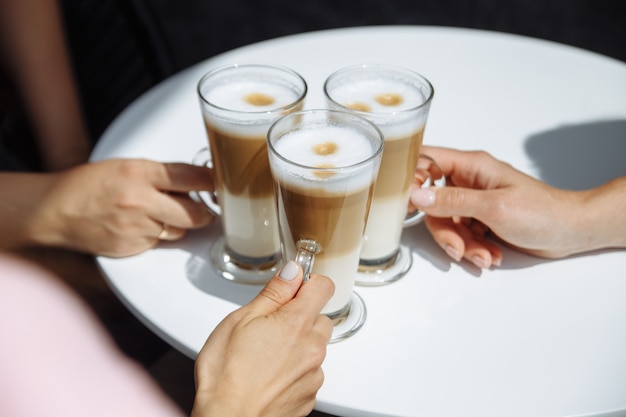 Drei Mädchen halten ein Glas duftenden Lattekaffee in den Händen