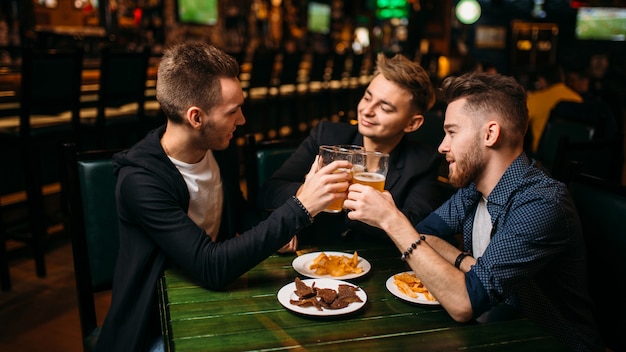 Drei Männer hoben ihre Gläser mit Bier, um in einer Sportkneipe den Sieg zu erringen