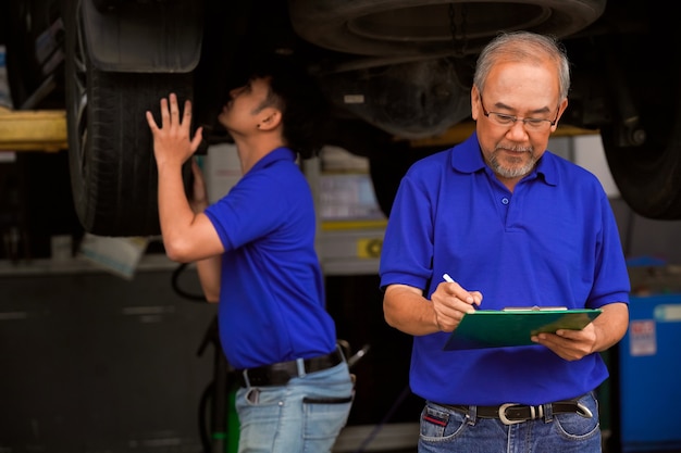 Drei männliche Automechaniker überprüfen mit Laptops die Federung und den Zustand der Reifen.