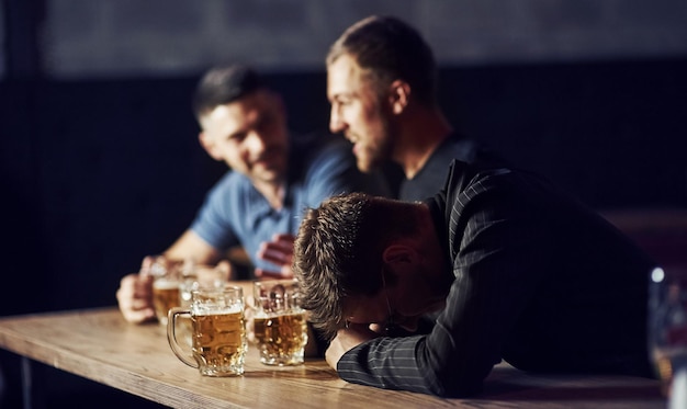 Drei männliche Freunde in der Bar unterstützen den traurigen Freund Einheit der Menschen mit Bier auf dem Tisch