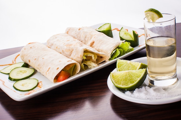 Foto drei mexikanische tortillas wickeln sich mit tequila, zitrone und salz auf holztisch, gegen weiße oberfläche