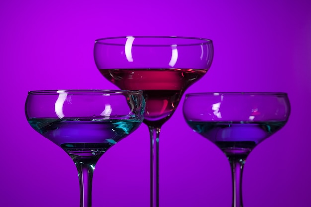 Drei mit Wein gefüllte Gläser stehen auf dem Tisch im Studio. Lebendige helle farbige Beleuchtung. Trendige 2018 Ultra Violet Glühbirne. Kunstdekoration mit mystischem Farbton