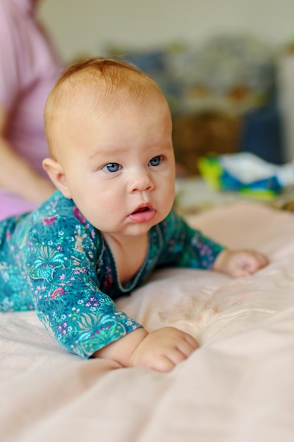 Drei Monate altes Baby liegt auf dem Bett und hält ihren Kopf.