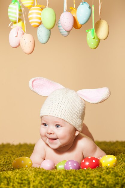 Drei monate baby auf dem bauch liegend als osterhase im gras mit eiern