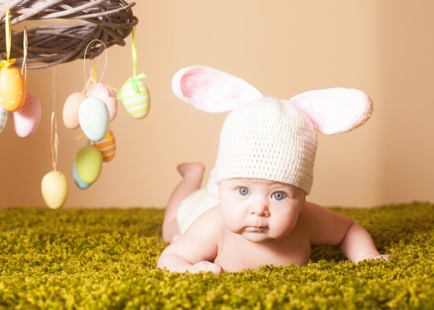 Drei Monate Baby auf dem Bauch liegend als Osterhase im Gras mit Eiern