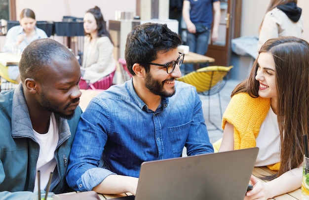 Drei multikulturelle glückliche Studenten, die zusammen im Café im Freien lernen